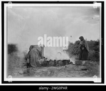 Bruciatori di ceramica a Santa Clara, c1905. La fotografia mostra due donne, probabilmente Tewa, che curano una fossa di fuoco, Santa Clara Pueblo, New Mexico. Foto Stock