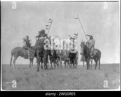 Atsina Warriors, c1908. Diversi guerrieri Atsina a cavallo, alcuni con personale piumato e uno con copricapo. Foto Stock