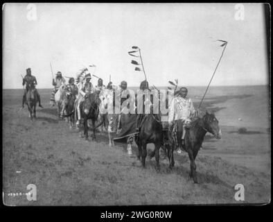 Sulla via della guerra - Atsina, c1908. Piccolo gruppo di uomini Atsina a cavallo, alcuni portavano del personale con piume, uno che indossava un cofano da guerra. Foto Stock