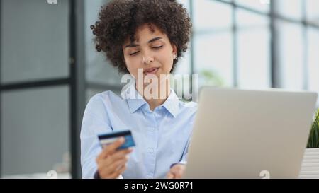 Una ragazza in un ufficio moderno paga gli acquisti su Internet utilizzando una carta di credito Foto Stock