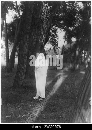 In attesa nella foresta-Cheyenne, c1910. L'uomo Cheyenne, in piedi nella foresta, è coperto di coperta bianca tranne che per gli occhi e il naso, sperando di incontrare la sua ragazza. Foto Stock