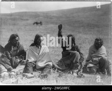 Incenso-Atsina, c1908. Quattro uomini Atsina, ciascuno avvolto in una coperta, seduti a terra, uno con braccio e pugno sollevati verso l'alto, uno con un'ala. Foto Stock