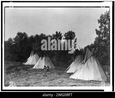 Un campo di Assiniboin contenente quattro tepee con indiani seduti a terra, c1908. Foto Stock