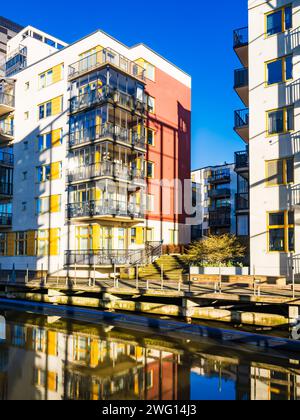 L'immagine cattura le vivaci facciate dei moderni condomini che riflettono sulle acque tranquille di un canale urbano in una giornata di sole. Foto Stock