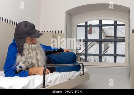 Un uomo triste con la barba giace su una cuccetta in una cella della prigione Foto Stock