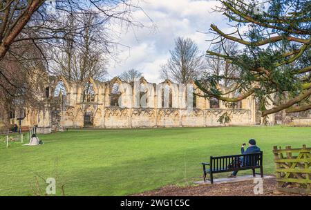 Le rovine dell'abbazia di St Marys dell'XI secolo nel parco di un parco municipale. C'è un prato di fronte all'abbazia e un uomo siede una panchina in t Foto Stock