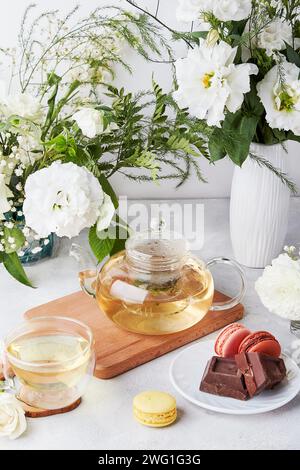 Tavolo estetico mattutino. Teiera, tazza, macaron, cioccolato, fiori bianchi - tempo per te stesso. Concetto di stile di vita Foto Stock