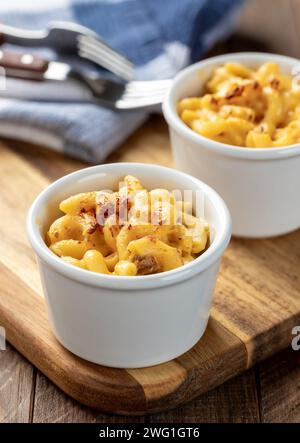 Macaroni e formaggio al forno in una tazza bianca su un asse di legno Foto Stock