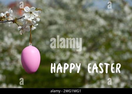 Biglietto di auguri con auguri di buona Pasqua. Primo piano dell'uovo decorativo di Pasqua sul ramo sullo sfondo di alberi fioriti. Concetto di vacanza. Religio Foto Stock