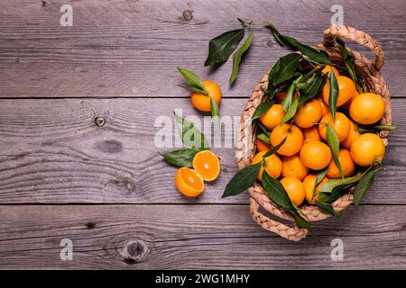 sul rustico tavolo in legno, vista dall'alto, un cesto di clementine con foglie. Foto Stock
