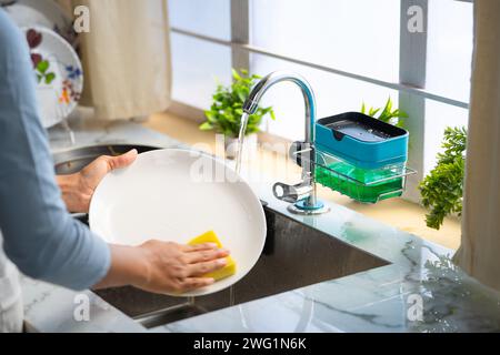Primo piano di una donna che lava le mani dei piatti o degli utensili in cucina usando sapone liquido - concetto di lavoro domestico domestico e lavoro domestico di routine Foto Stock