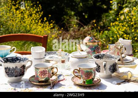 'Un tea party all'aperto ambientato su uno sfondo di fiori selvatici caratterizzato da una vasta gamma di porcellane vintage. Foto Stock