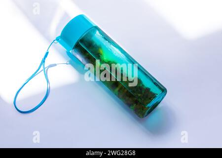 Tè verde freddo in bottiglia turchese riutilizzabile su sfondo bianco pastello con messa a fuoco selettiva. Rinfrescante mockup con marchio di bevande analcoliche ghiacciate. Guarire Foto Stock