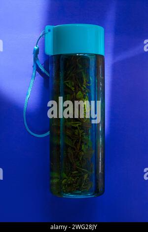 Preparare il tè verde freddo in una bottiglia riutilizzabile turchese su sfondo blu pastello. Rinfrescante mockup con marchio di bevande analcoliche ghiacciate. Dieta sana. Zero wa Foto Stock