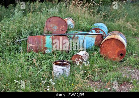 vecchie botti di olio arrugginite giacciono su un prato verde con erba alta Foto Stock