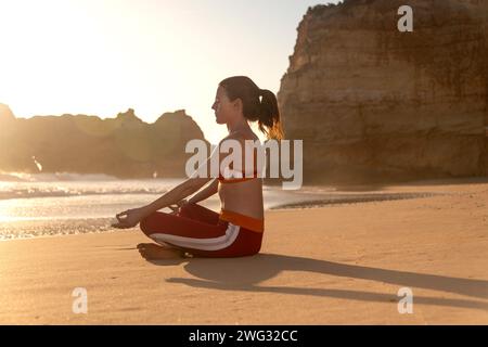 Donna sportiva seduta sulla spiaggia che medita. Surfisti o nuotatori. Foto Stock