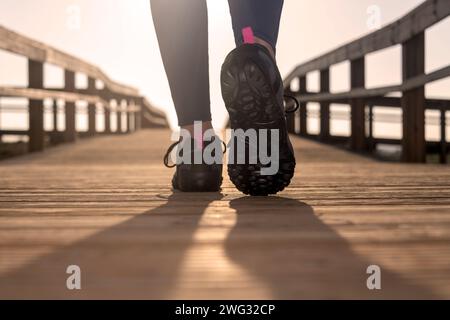 primo piano di una donna che indossa scarpe da passeggio, che cammina lungo una passerella di legno al sole Foto Stock