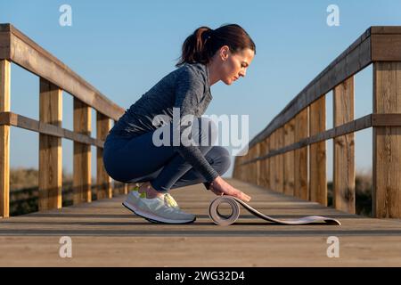 Primo piano di una donna che stende un tappetino da ginnastica su una passerella al sole Foto Stock