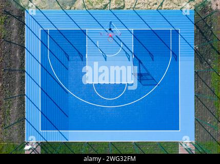 Vista dall'alto del campo da pallacanestro. Campo sportivo blu con lunghe ombre alla luce del giorno dalla vista aerea dei droni. Foto Stock