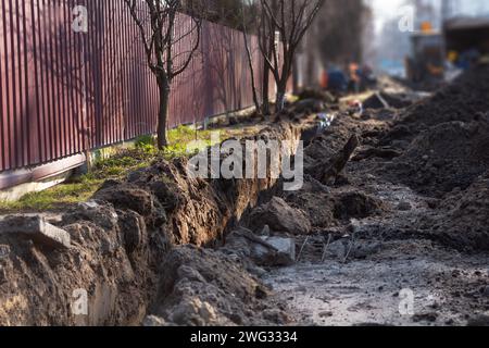 Lavori di terra. Una profonda e lunga trincea scavata nel terreno per la posa di cavi e tubi. Settore delle telecomunicazioni. Foto Stock