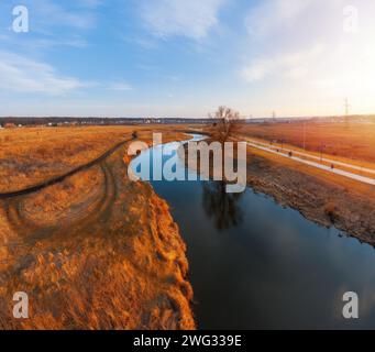 Fiume tortuoso nel campo con erba secca. Paesaggio autunnale con fiume che gira, prato arancione e albero solitario sulla riva dalla vista aerea. Foto Stock