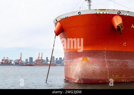 La prua di una nave portacontainer ancorata nel porto di Vancouver con lo skyline di Vancouver, British Columbia sullo sfondo. Foto Stock