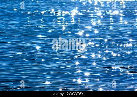 Superficie di acqua blu con raggi solari e bokeh, sfondo astratto Foto Stock