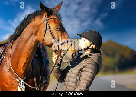 Un ritratto della testa di un cavallo contro un cielo blu, il cavaliere si trova accanto al cavallo. Una soleggiata giornata autunnale nella natura. Foto Stock