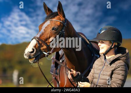 Un ritratto della testa di un cavallo contro un cielo blu, il cavaliere si trova accanto al cavallo. Una soleggiata giornata autunnale nella natura. Foto Stock