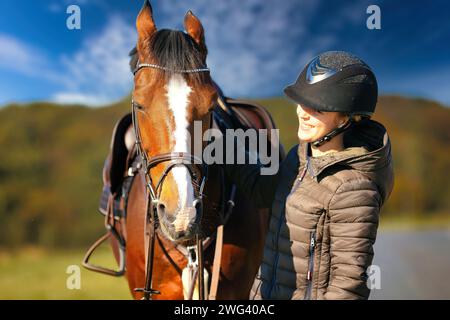 Un ritratto della testa di un cavallo contro un cielo blu, il cavaliere si trova accanto al cavallo. Una soleggiata giornata autunnale nella natura. Foto Stock