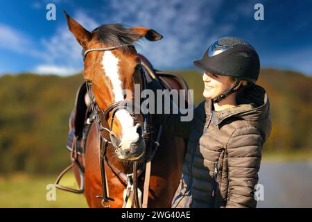 Un ritratto della testa di un cavallo contro un cielo blu, il cavaliere si trova accanto al cavallo. Una soleggiata giornata autunnale nella natura. Foto Stock