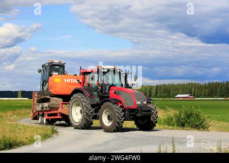 Jokioinen, Finlandia - 13 luglio 2019: Il trattore agricolo Red Valtra T151 trasporta l'escavatore Hitachi Zaxis 130 LCN lungo le strade di campagna nelle giornate di sole dell'estate. Foto Stock