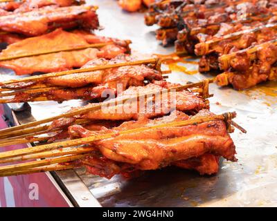 Il Chciken veniva preparato alla brace tra due bastoncini di bambù in un mercato della Thailandia. Profondità di campo ridotta. Foto Stock