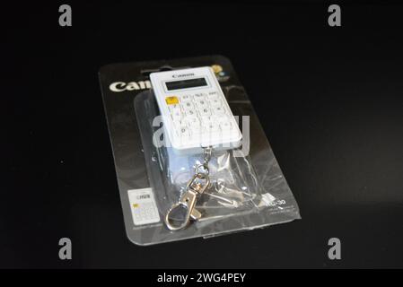 Piccola calcolatrice dal design elegante e bianca su una superficie nera lucida. Foto Stock