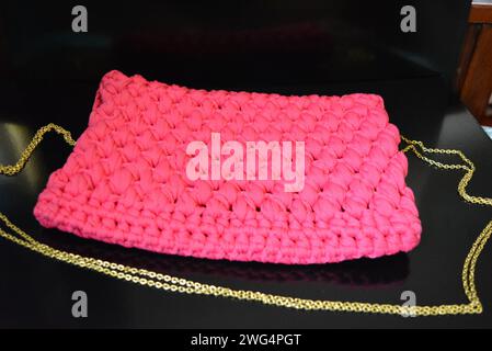 Su uno sfondo nero lucido è presente una borsa in tessuto rosa da donna sulla spalla con una culla dorata, un apriscatole e un riflesso. Foto Stock
