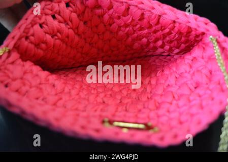 Su uno sfondo nero lucido è presente una borsa in tessuto rosa da donna sulla spalla con una culla dorata, un apriscatole e un riflesso. Foto Stock