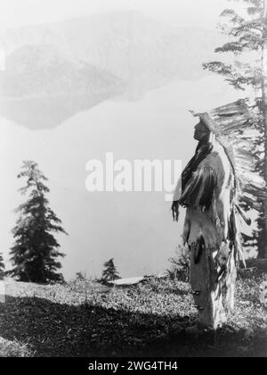 Pregare gli spiriti al Crater Lake-Klamath, c1923. Capo indiano di Klamath in piuma che si trova sulla montagna che si affaccia sul lago Crater, Oregon. Foto Stock