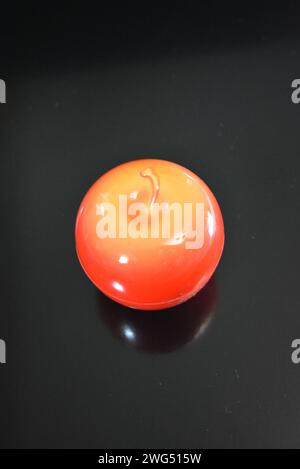 Su una superficie nera lucida si trova una mela di plastica di colore rosso brillante in cui è confezionata una crema di pelle e viso. Foto Stock