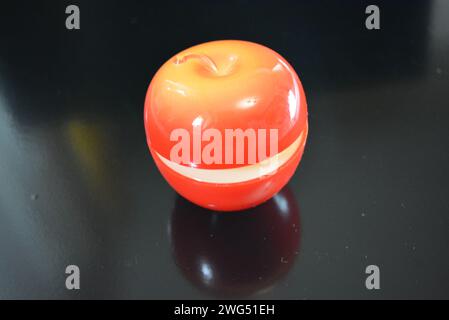 Su una superficie nera lucida si trova una mela di plastica di colore rosso brillante in cui è confezionata una crema di pelle e viso. Foto Stock