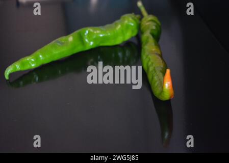 Peperoncino verde amaro fresco e succoso, peperoncino appoggiato su una superficie nera lucida con riflessi ripetuti. Foto Stock