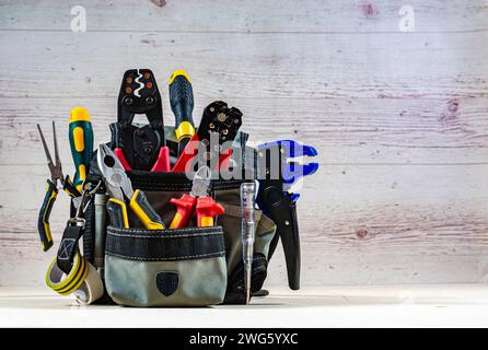 Borsa per elettricisti con utensili elettrici professionali. Pinze, tagliafili, spelafili, cacciaviti, tester, pinze crimpatrici. Sfondo in legno chiaro. Foto Stock