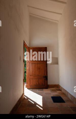 Corridoio con una porta aperta in legno e un piccolo tappeto, illuminato dal sole del mattino, in una fattoria sulle Ande orientali della Colombia centrale. Foto Stock