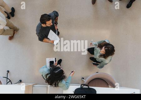 Una foto aerea cattura un gruppo di professionisti in un ambiente aziendale rilassato, impegnandosi in una discussione con documenti e tablet digitali in mano. Foto Stock