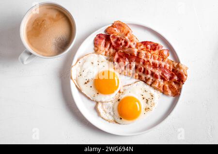 Colazione con uova fritte e pancetta da vicino. Uova fritte al sole con pancetta sul piatto e tazza di caffè del mattino, sano pasto keto. Foto Stock