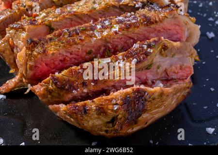 Primo piano di un taglio di manzo su un piatto nero con sale. Il taglio è di circa 2 cm e ha una consistenza leggermente marmorizzata. La carne viene cotta a media Foto Stock