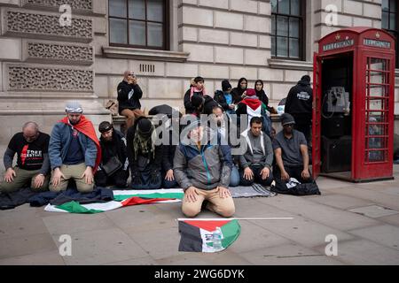 Mentre i sostenitori filo-palestinesi marciano di nuovo attraverso il centro di Londra per chiedere un cessate il fuoco permanente a Gaza, gli uomini musulmani pregano accanto a una cabina telefonica a Whitehall, il 3 febbraio 2024, a Londra, in Inghilterra. Foto Stock