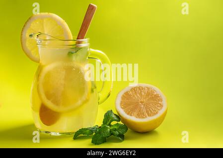 Caraffa di limonata con fette di limone e un cucchiaio di legno accanto alla menta e mezzo limone. Foto Stock