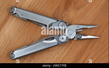 Un moderno coltello multifunzione pieghevole aperto realizzato in ferro grigio su fondo in legno. MultiTool con attrezzi e pinze estesi. Compatto e portatile Foto Stock