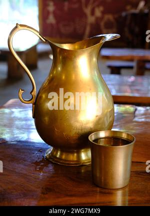 Caraffa d'acqua in ottone e vetro riempiti d'acqua su un piano di legno Foto Stock