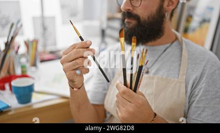 Bellissimo artista ispanico che tiene in mano pennelli in un ambiente creativo. Foto Stock